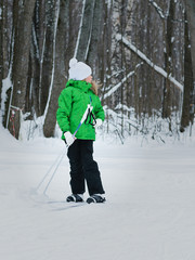 The girl in the green jumpsuit looks back at the path on skis.