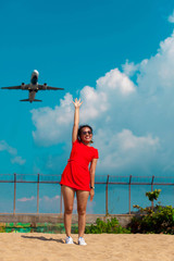 Asian woman jumping raised up hands celebrate with airplane flying above tropical beach on blue sky background 