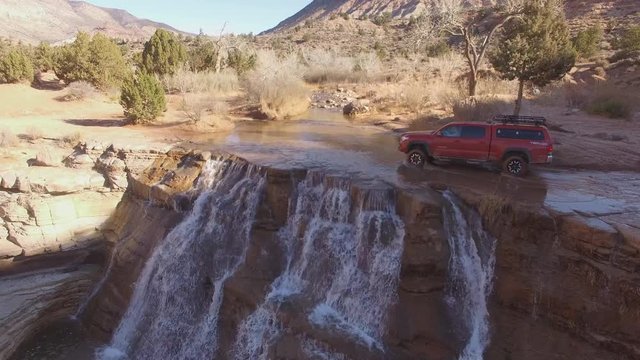 Flying over truck driving through river at the top of Toquerville Falls in the Utah desert.