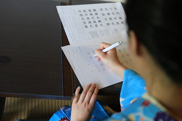 a woman in kimono is writing kanji with pen