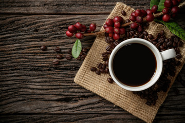 A cup of coffee on wooden desk with red ripe coffee beans.