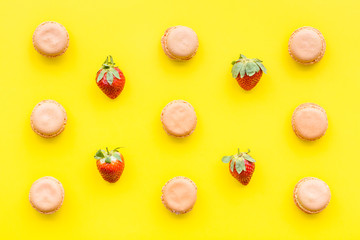 Fototapeta na wymiar Fresh ripe strawberry. Pattern with sweets macarons on yellow pastel background top view copy space