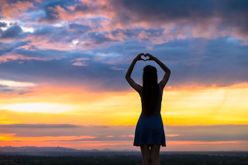 Woman making heart of hands at sunset