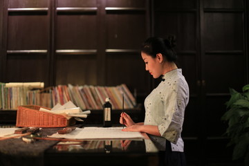 a woman in Chinese traditional costume is practicing Chinese traditional calligraphy with brush  - obrazy, fototapety, plakaty