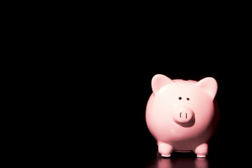 Simple Pink Piggy Bank on a Black Table in a Black Room - Savings can by ominous and difficult