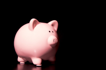 Simple Pink Piggy Bank on a Black Table in a Black Room - Savings can by ominous and difficult