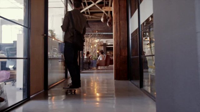 Man skateboarding in modern office and meeting his team. Casual businessman skating through his startup office with colleagues sitting in lobby.
