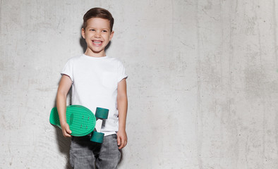 Cute smiling guy with skateboard in hand against gray wall. Portrait of skater boy in white T-shirt, concrete wall on background with copy space. © deniskomarov