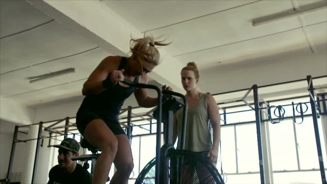 Fitness woman spinning on stationary bike in gym with personal coach. Strong female athlete doing indoor cycling during gym training class.