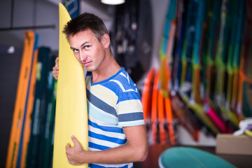 male is posing with surfboard in store on the beach.