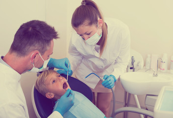 Fototapeta premium Stomatologist man with woman assistant are diagnosticating to young patient which is sitting