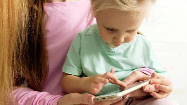 Happy young mother and daughter playing, drawing, playing games on your smartphone braid braids, read.