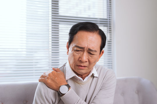 Elderly man suffering from shoulder pain sitting on a sofa in the living room