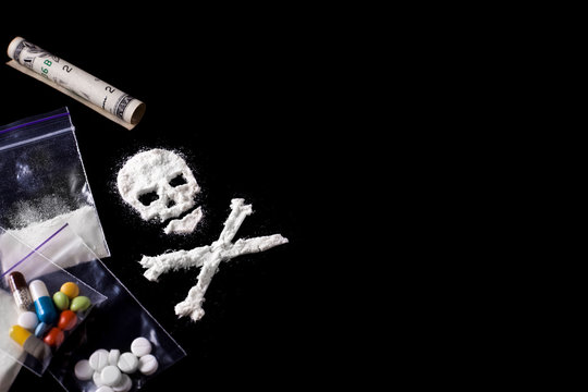 Drug dependence Kills. A line of cocaine in the form of a skull and a roll of a dollar, sachets with a dose, pills. Black background. Addiction concept. Copy space for text