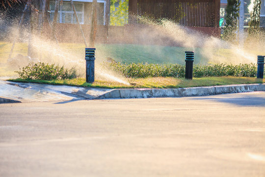 Automatic Lawn Sprinklers Watering Over Green Grass In The Garden