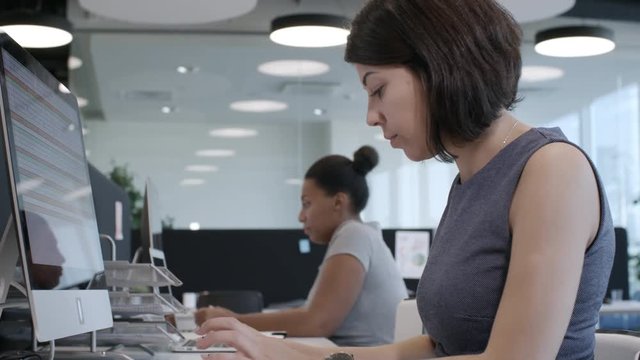 PAN shot of African and Latin businesswomen sitting at desks and working on computers in modern open space office