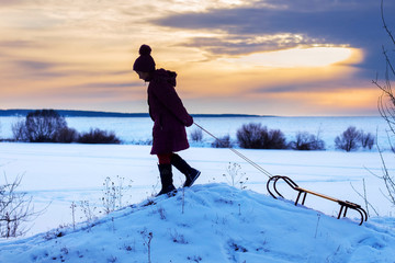 girl with sleds climbing a hill, winter evening, sunset, healthy lifestyle_