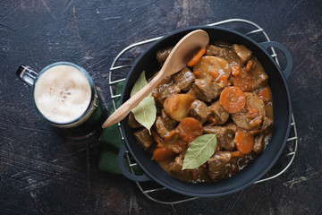 Cast-iron pan with traditional Irish meal of beef and beer stew, dark brown stone background, top view, studio shot