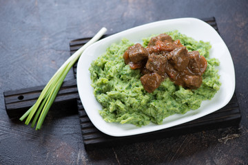White plate with Irish colcannon and beef and beer stew on a black wooden serving board, one of traditional dishes for Saint Paddy's Day