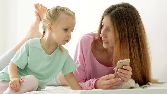 Happy young mother and daughter playing, drawing, playing games on your smartphone braid braids, read.