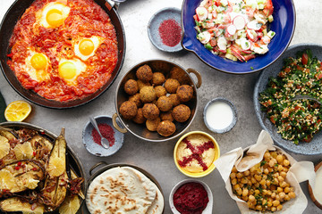 Overhead image of traditional jewish and middle eastern food: falafel, fattoush, tabouli, shakshuka, balila, hummus, roasted eggplants and spicy beetroot dip. Israeli cuisine concept