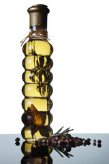 An interesting bottle of oil and a plant inside, is visible through, beside a hill of spices from a sprig of rosemary and peppers