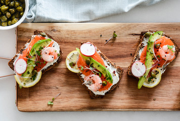 Smorrebrod, traditional Danish open sanwiches, dark rye bread with salmon, avocado, shrimp and micro-green. Top view.