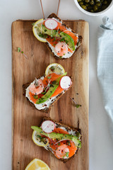 Smorrebrod, traditional Danish open sanwiches, dark rye bread with salmon, avocado, shrimp and micro-green. Top view.