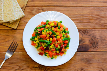 Winter vegetable mix stew on a serving plate and wooden table. Simple stewed carrots, green beans, red beans, peas, corn, pepper and onions slices. Healthy vegetable stew recipe. Top view