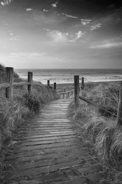 Beautiful black and white sunrise landscape image of sand dunes system over beach with wooden boardwalk