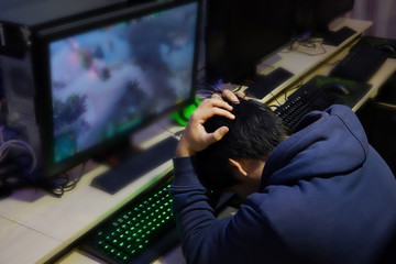 Stressed gamer while playing computer games until morning at internet cafe, game addiction concept,...