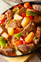 Stew beef with potatoes, peppers, peas, tomatoes and carrots in a large ally on a plate on the table. vertical