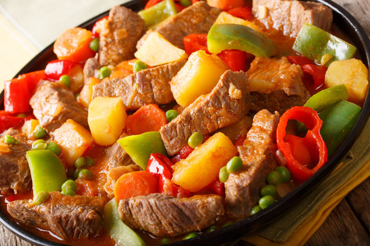Slow cooked beef with potatoes, peppers, peas, tomatoes and carrots in a spicy sauce close-up. horizontal