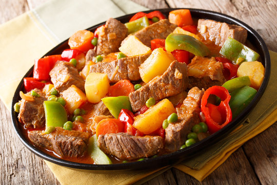 Caldereta beef with potatoes, pepper, peas, tomatoes and carrots in a spicy sauce close-up on a plate . horizontal