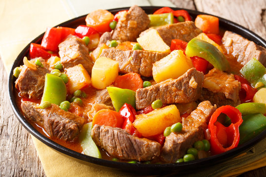 Organic food: beef with potatoes, pepper, peas, tomatoes and carrots in a spicy sauce close-up on a plate . horizontal