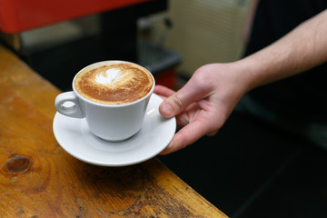 Hand barista holding and serving cup of coffee.