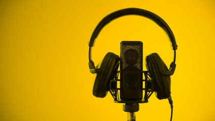 Professional microphone and headphones on yellow background