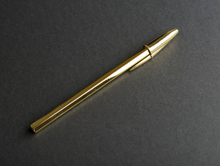 Golden ballpoint pen on black background. Copy space.