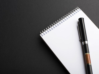 Black ballpoint pen on notepad with empty page, on black background. Copy space. Mockup.