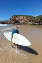 Young boy leaves the surf carrying his surfboard at Caves Beach - New South Wales Australia. Caves beach is a popular beach south of Newcastle
