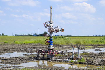 Oil well after repair in mud and puddles. Oil well wellhead equipment. Hand valve with handwheel...