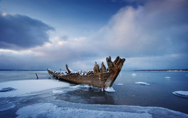 Old wooden shipwreck in ice at sea. Winter on the water at night