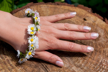 Female hand with daisy flower bracelet in the sun with a wooden surface