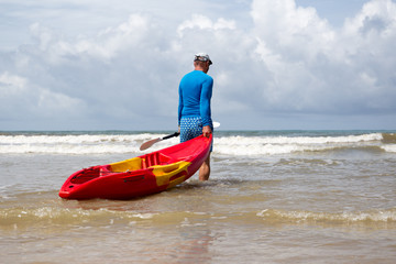 Fototapeta premium Man pulling kayak to the sea wave on vacation