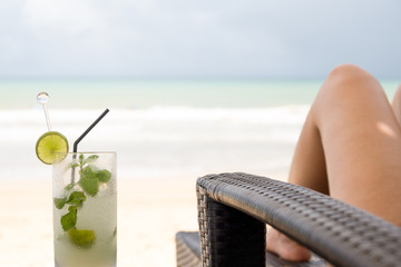 Glass of mojito drink and  woman legs on the beach