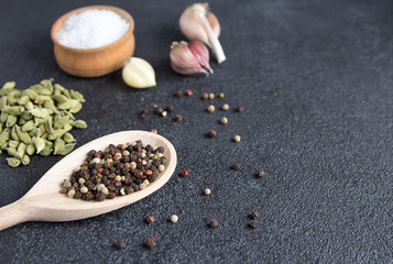 Cardamom, pepper, garlic, salt on black stone background.