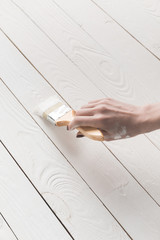 cropped image of woman painting wooden surface with white paint