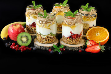 Granola, slices of different fresh fruits, yogurt, honey in jars isolated on black background.
