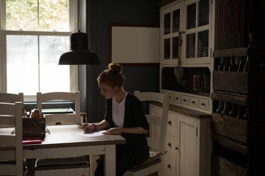 Young woman sitting at table writing a letter 