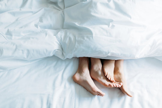 cropped image of boyfriend and girlfriend lying in bed under blanket